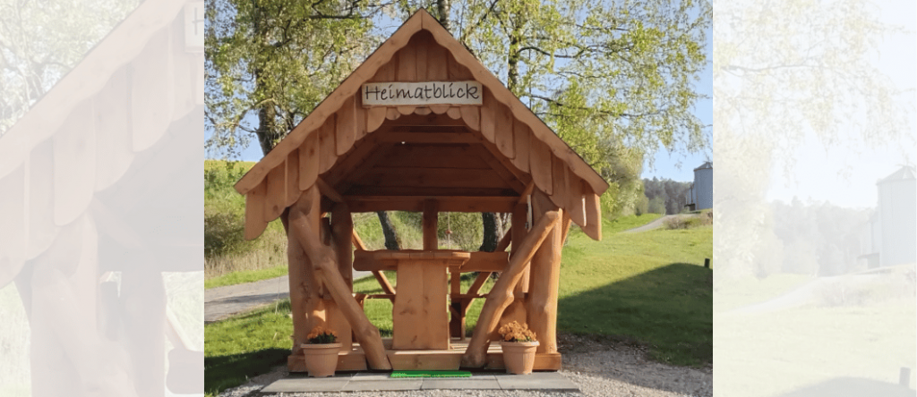 Rustikaler Gartenpavillon aus Holz auf einem ländlichen Grundstück mit Scheune und grüner Wiese