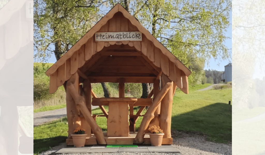Rustikaler Gartenpavillon aus Holz auf einem ländlichen Grundstück mit Scheune und grüner Wiese